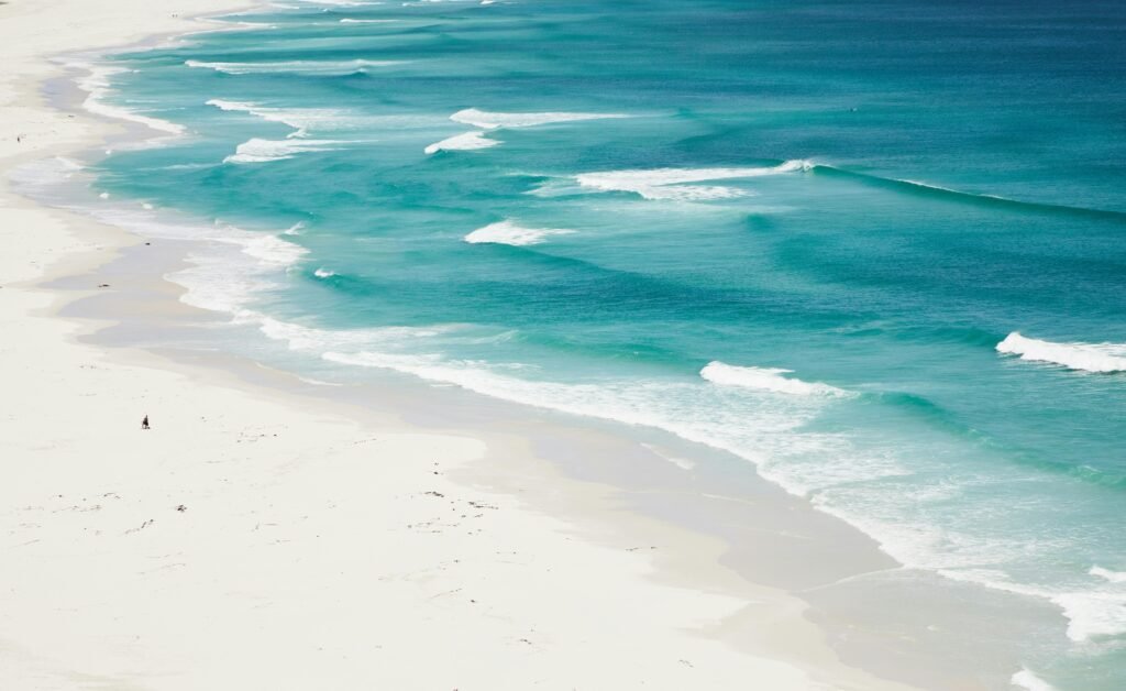 A serene aerial view of turquoise ocean waves gently washing over a pristine white sandy beach.